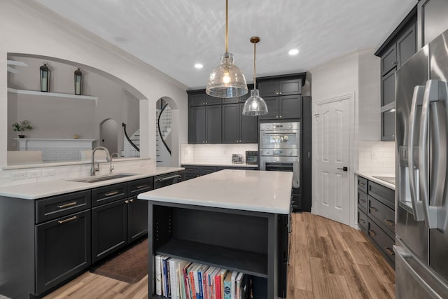 kitchen with appliances with stainless steel finishes, a sink, backsplash, ornamental molding, and light wood finished floors