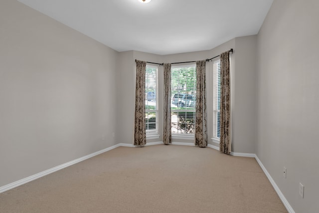 spare room featuring light carpet and baseboards