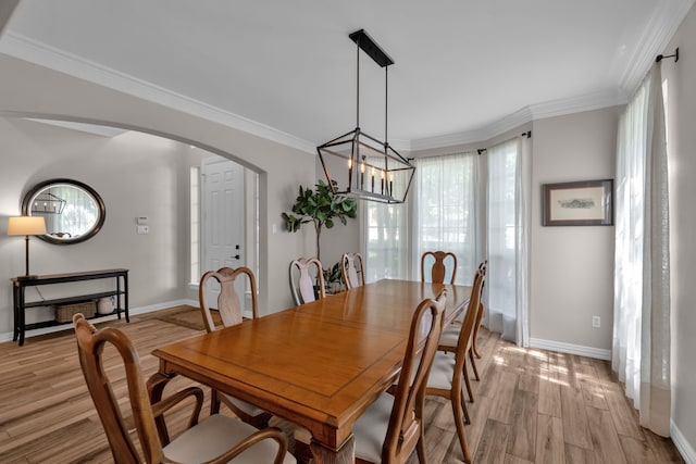dining room featuring light wood-style flooring, arched walkways, baseboards, ornamental molding, and a chandelier