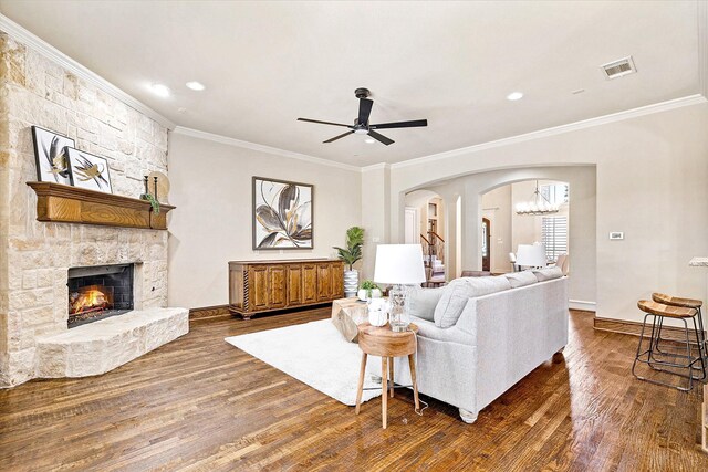 living room featuring crown molding, dark wood-type flooring, arched walkways, a stone fireplace, and baseboards