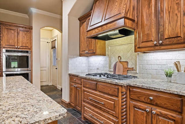 kitchen with stainless steel appliances, arched walkways, crown molding, light stone countertops, and baseboards