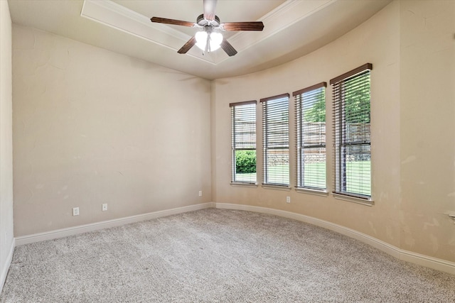 empty room with carpet flooring, a raised ceiling, baseboards, and a ceiling fan