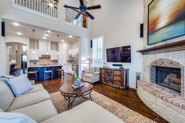 3020 Speyburn, The Colony, TX 75056 - living area featuring dark wood-type flooring, ceiling fan, a high ceiling, a fireplace with raised hearth, and arched walkways