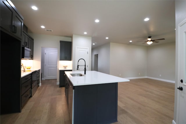 914 S Brazos St, Weatherford, TX 76086 - kitchen featuring a sink, stainless steel microwave, light wood-style floors, ceiling fan, and a center island with sink