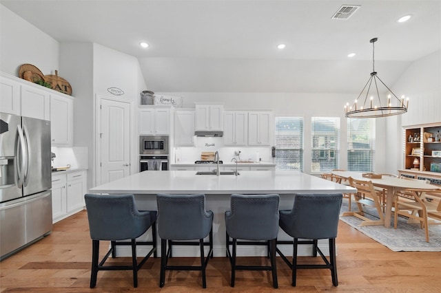 1105 Collared Dove Dr, Little Elm, TX 75068 - kitchen featuring appliances with stainless steel finishes, vaulted ceiling, white cabinets, an island with sink, and a breakfast bar