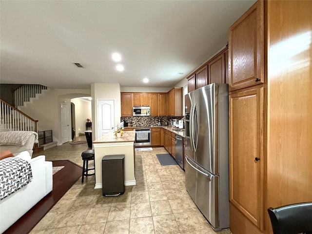8608 Davis Dr, Frisco, TX 75036 - kitchen with appliances with stainless steel finishes, open floor plan, arched walkways, decorative backsplash, and brown cabinets