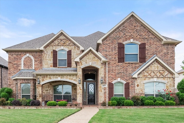 2855 England Pkwy, Grand Prairie, TX 75054 - french country style house featuring stone siding, a front lawn, roof with shingles, and brick siding