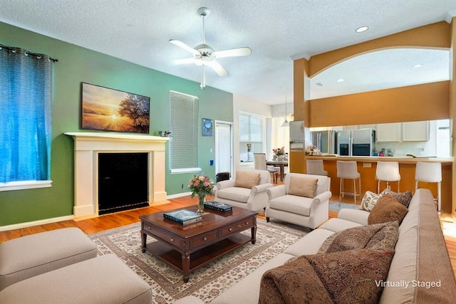 1325 Bentley Dr, Carrollton, TX 75006 - living room featuring light wood-style floors, ceiling fan, a textured ceiling, baseboards, and a fireplace with flush hearth