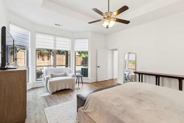 bedroom featuring multiple windows, wood finished floors, a tray ceiling, and ceiling fan