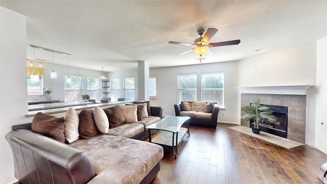 2225 Marion Dr, Mckinney, TX 75072 - living area featuring a textured ceiling, ceiling fan, a tiled fireplace, hardwood / wood-style floors, and baseboards