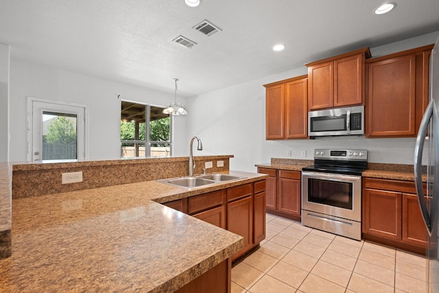 303 Stonegate Blvd, Alvarado, TX 76009 - kitchen featuring appliances with stainless steel finishes, a sink, brown cabinets, light tile patterned floors, and hanging light fixtures