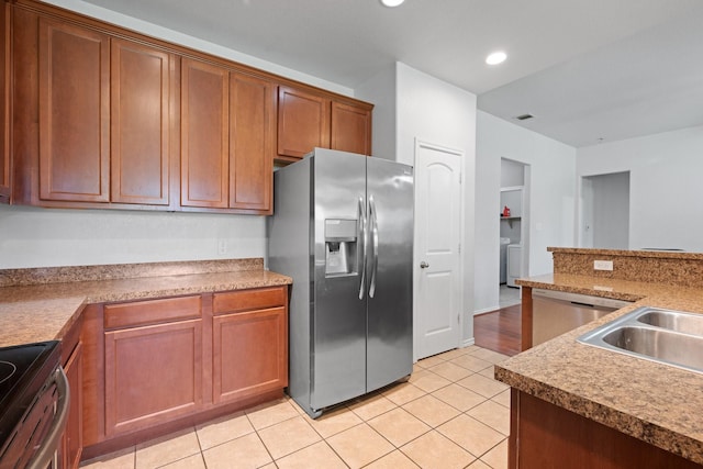 303 Stonegate Blvd, Alvarado, TX 76009 - kitchen featuring stainless steel appliances, washer / dryer, light tile patterned floors, a sink, and brown cabinetry