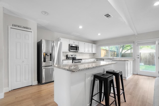 kitchen with appliances with stainless steel finishes, light wood-style floors, a center island, white cabinets, and light stone counters