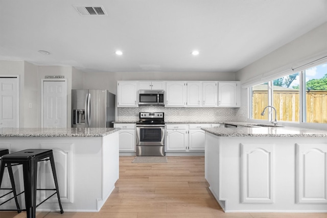 kitchen with stainless steel appliances, a sink, white cabinetry, light stone countertops, and recessed lighting