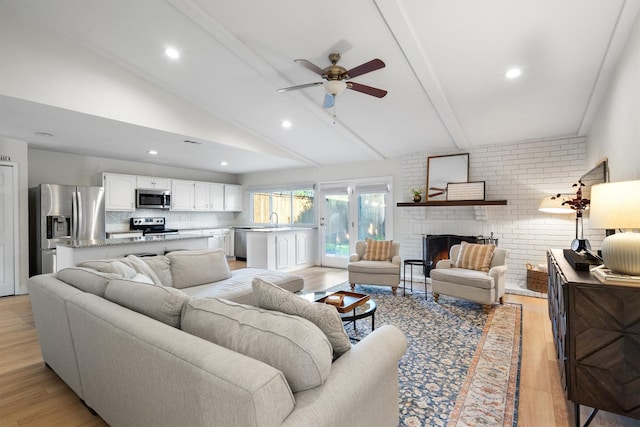 living area with beam ceiling, ceiling fan, light wood-style floors, a brick fireplace, and high vaulted ceiling