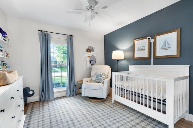 carpeted bedroom featuring a crib, baseboards, and a ceiling fan