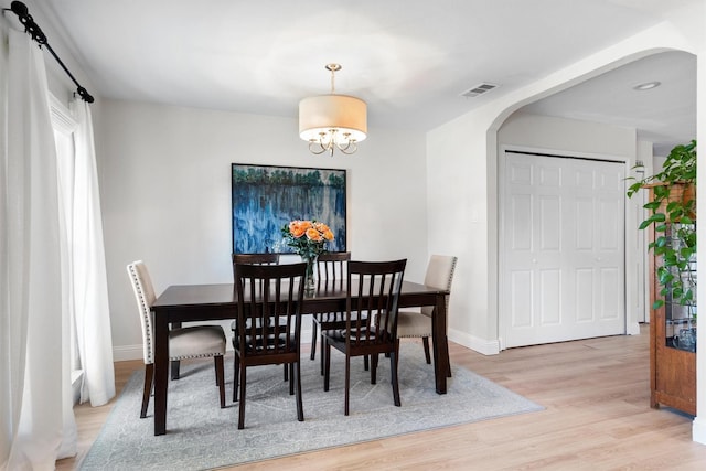 dining area featuring arched walkways, light wood-style floors, baseboards, and a chandelier