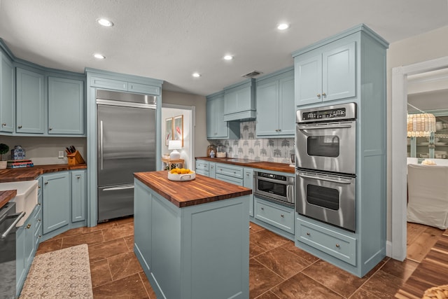 3304 Bowden Hill Ln N, Colleyville, TX 76034 - kitchen featuring butcher block countertops, appliances with stainless steel finishes, a kitchen island, decorative backsplash, and blue cabinetry