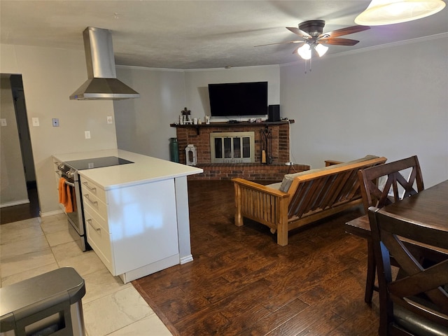 kitchen with stainless steel range with electric cooktop, wall chimney range hood, ceiling fan, white cabinetry, and light countertops