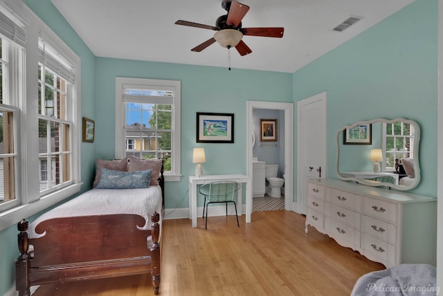 bedroom featuring light wood finished floors, baseboards, ensuite bathroom, and a ceiling fan