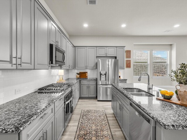 571 Mckenna Dr, Fate, TX 75087 - kitchen featuring stainless steel appliances, gray cabinetry, stone countertops, tasteful backsplash, and light wood-type flooring