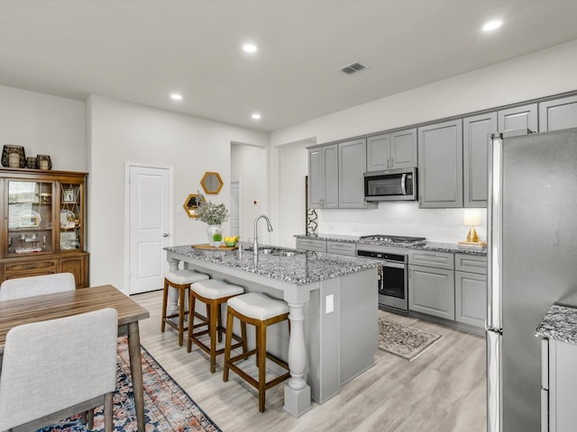 571 Mckenna Dr, Fate, TX 75087 - kitchen with appliances with stainless steel finishes, gray cabinetry, a sink, light stone counters, and light wood-style floors