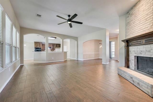 712 Britain Way, Wylie, TX 75098 - unfurnished living room featuring ceiling fan, a brick fireplace, wood finished floors, and arched walkways
