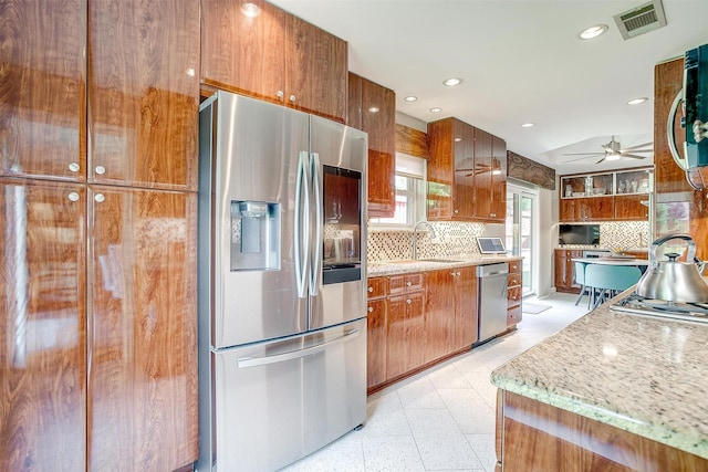 kitchen with appliances with stainless steel finishes, a sink, brown cabinetry, backsplash, and ceiling fan