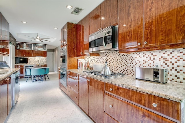 kitchen featuring appliances with stainless steel finishes, ceiling fan, decorative backsplash, light stone counters, and recessed lighting
