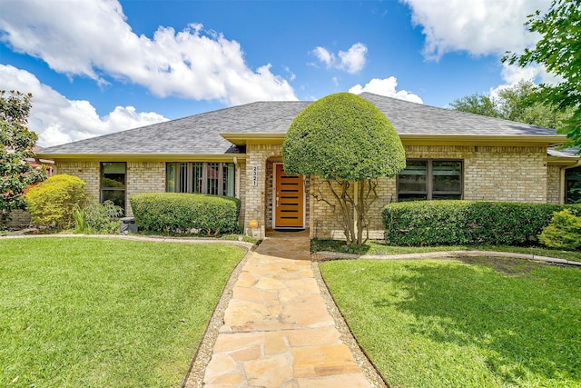 single story home with brick siding, a front yard, and a shingled roof