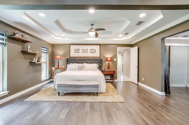 bedroom featuring a raised ceiling, wood finished floors, baseboards, and ornamental molding