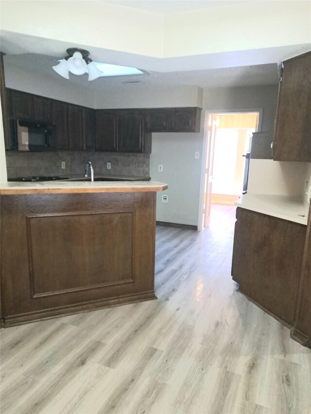 327 Trevino Trl, Lancaster, TX 75146 - kitchen with black microwave, light wood finished floors, tasteful backsplash, dark brown cabinets, and a ceiling fan
