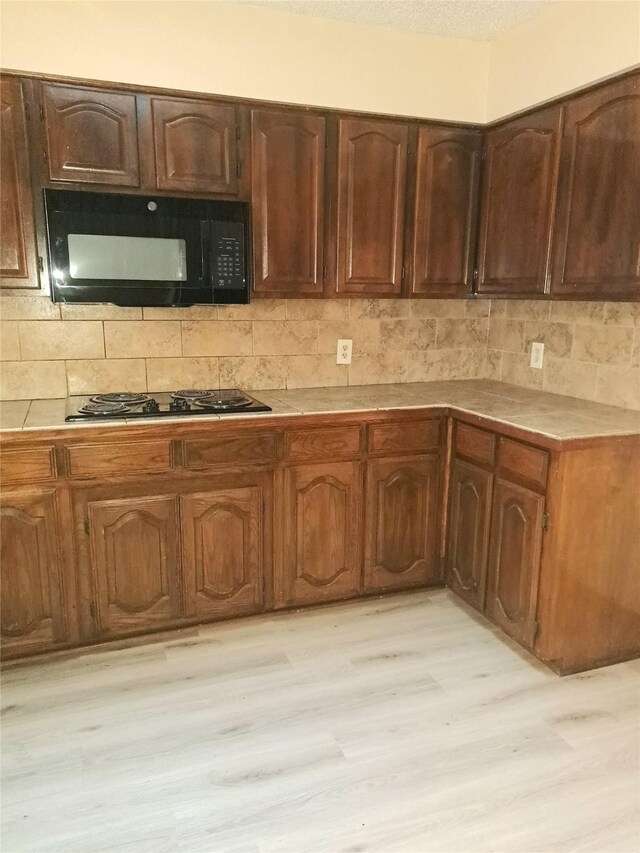 327 Trevino Trl, Lancaster, TX 75146 - kitchen with black appliances, light wood finished floors, tile countertops, and tasteful backsplash
