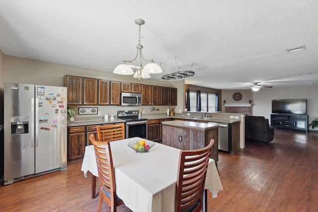 1554 Brandywine Ln, Little Elm, TX 75068 - kitchen with appliances with stainless steel finishes, a chandelier, a peninsula, dark wood-style flooring, and a center island