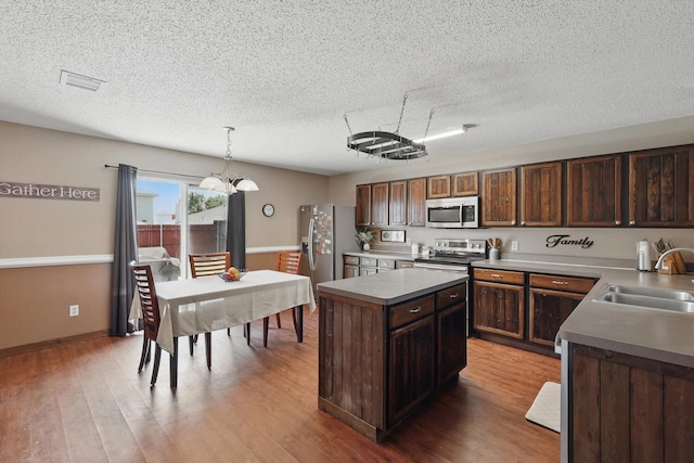 1554 Brandywine Ln, Little Elm, TX 75068 - kitchen featuring stainless steel appliances, a sink, a textured ceiling, wood finished floors, and a kitchen island