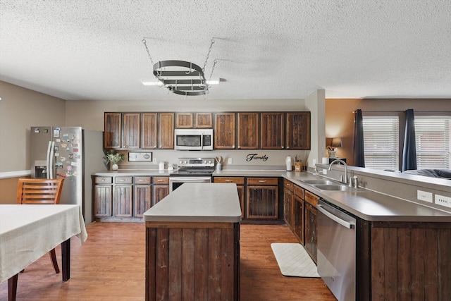 1554 Brandywine Ln, Little Elm, TX 75068 - kitchen featuring appliances with stainless steel finishes, a textured ceiling, a peninsula, a sink, and light wood-style flooring