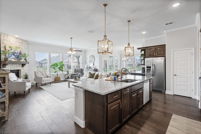 1037 Mickelson Dr, Granbury, TX 76048 - kitchen featuring appliances with stainless steel finishes, ornamental molding, a sink, dark brown cabinets, and a stone fireplace