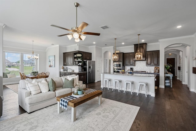1037 Mickelson Dr, Granbury, TX 76048 - living room featuring arched walkways, a chandelier, a ceiling fan, crown molding, and dark wood-style floors