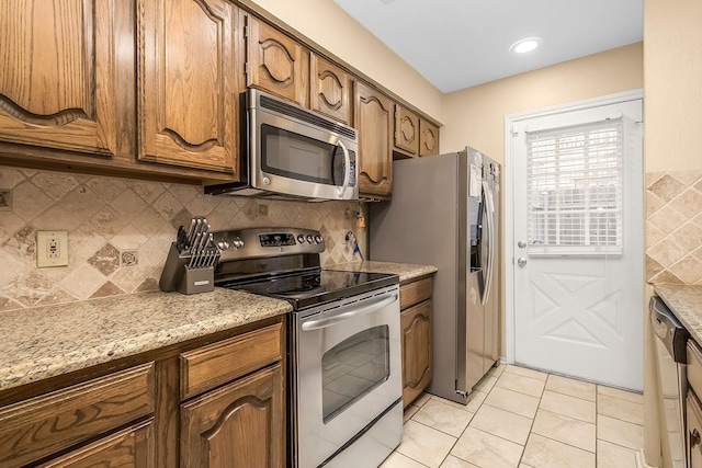 14333 Preston Rd Unit 2403, Dallas, TX 75254 - kitchen featuring stainless steel appliances, tasteful backsplash, light tile patterned floors, brown cabinets, and light stone counters