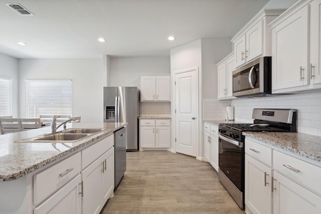 8580 Big Apple Dr, Fort Worth, TX 76179 - kitchen with stainless steel appliances, a sink, light wood-type flooring, white cabinetry, and decorative backsplash
