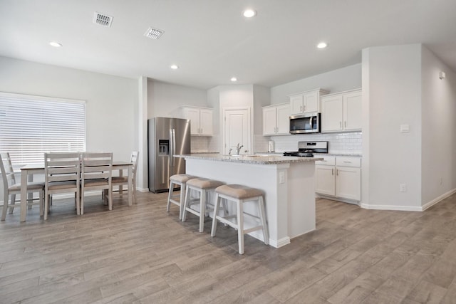 8580 Big Apple Dr, Fort Worth, TX 76179 - kitchen featuring appliances with stainless steel finishes, tasteful backsplash, light wood-type flooring, a center island with sink, and white cabinetry