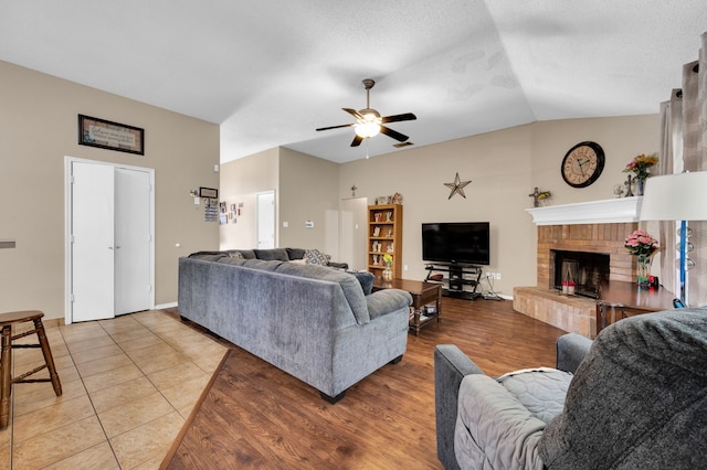 living area featuring vaulted ceiling, ceiling fan, light wood-type flooring, and a fireplace