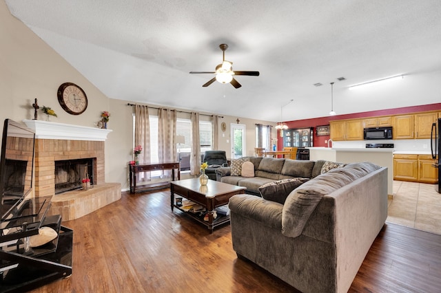 living area with vaulted ceiling, a ceiling fan, wood finished floors, and a brick fireplace