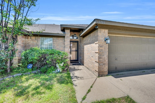 doorway to property featuring roof with shingles, an attached garage, and brick siding