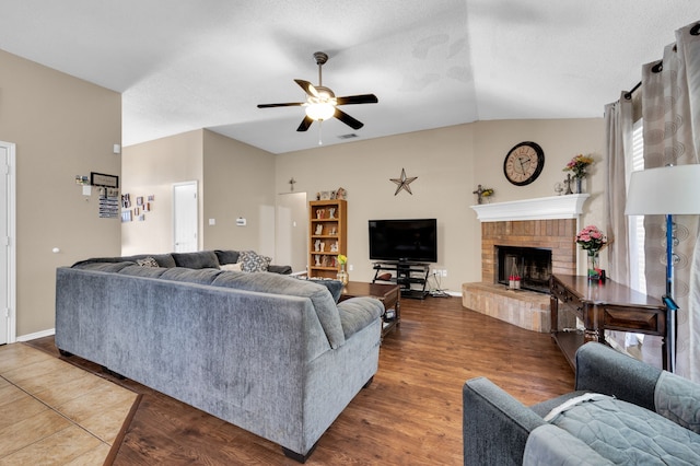 living area with a ceiling fan, vaulted ceiling, a fireplace, and wood finished floors
