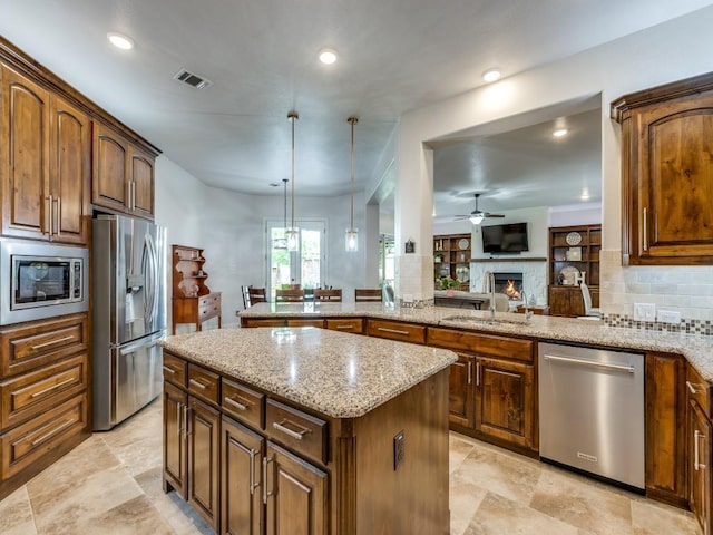 1141 Saint Peter Ln, Prosper, TX 75078 - kitchen with stainless steel appliances, a ceiling fan, a warm lit fireplace, light stone countertops, and backsplash