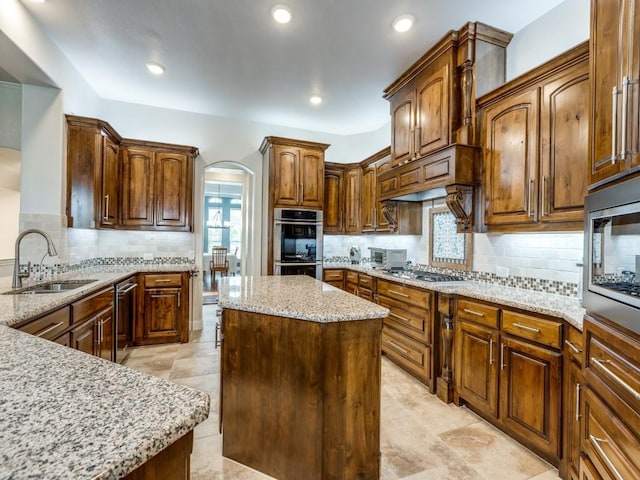 1141 Saint Peter Ln, Prosper, TX 75078 - kitchen with stainless steel appliances, arched walkways, tasteful backsplash, light stone countertops, and a kitchen island