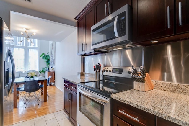 3100 Cole Ave Unit 203, Dallas, TX 75204 - kitchen featuring appliances with stainless steel finishes, a chandelier, light stone counters, dark brown cabinetry, and light tile patterned floors