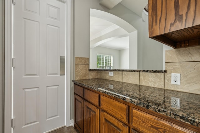 1968 Crowbridge Dr, Frisco, TX 75033 - kitchen featuring decorative backsplash, dark stone counters, arched walkways, ornamental molding, and brown cabinetry