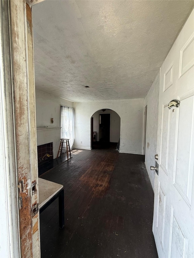 2911 Reed Ln, Dallas, TX 75215 - unfurnished living room with a textured ceiling, a brick fireplace, arched walkways, and hardwood / wood-style flooring
